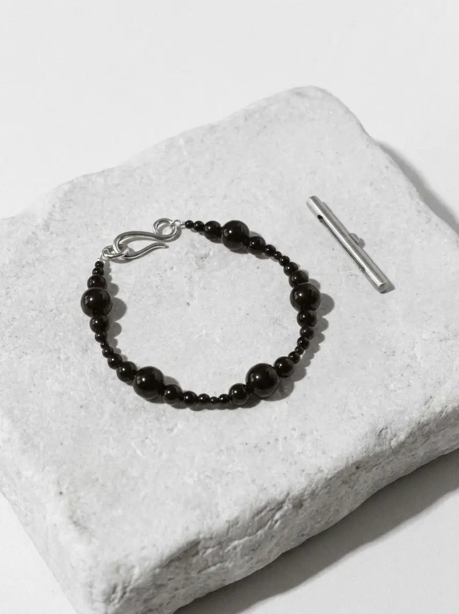 Gradient obsidian VOID bracelet on a white stone